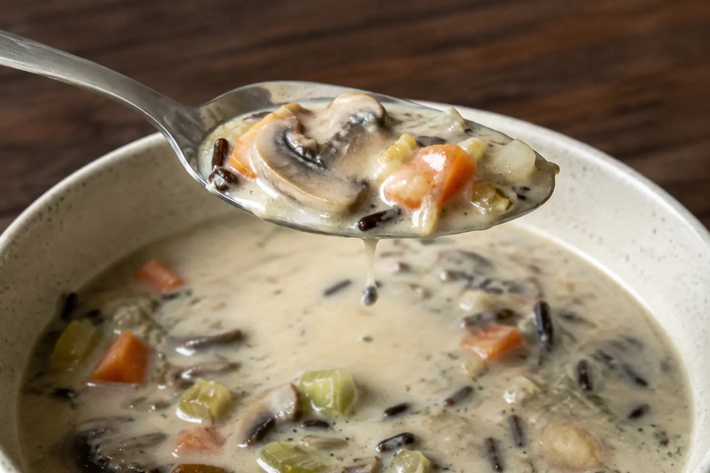 Spoonful of creamy mushroom wild rice soup showing tender vegetables, mushrooms, and chewy split grains.