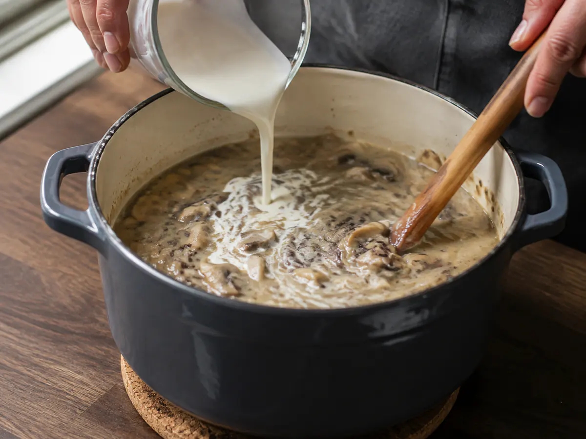 Cream being stirred into mushroom wild rice soup off the heat for a smooth finish.