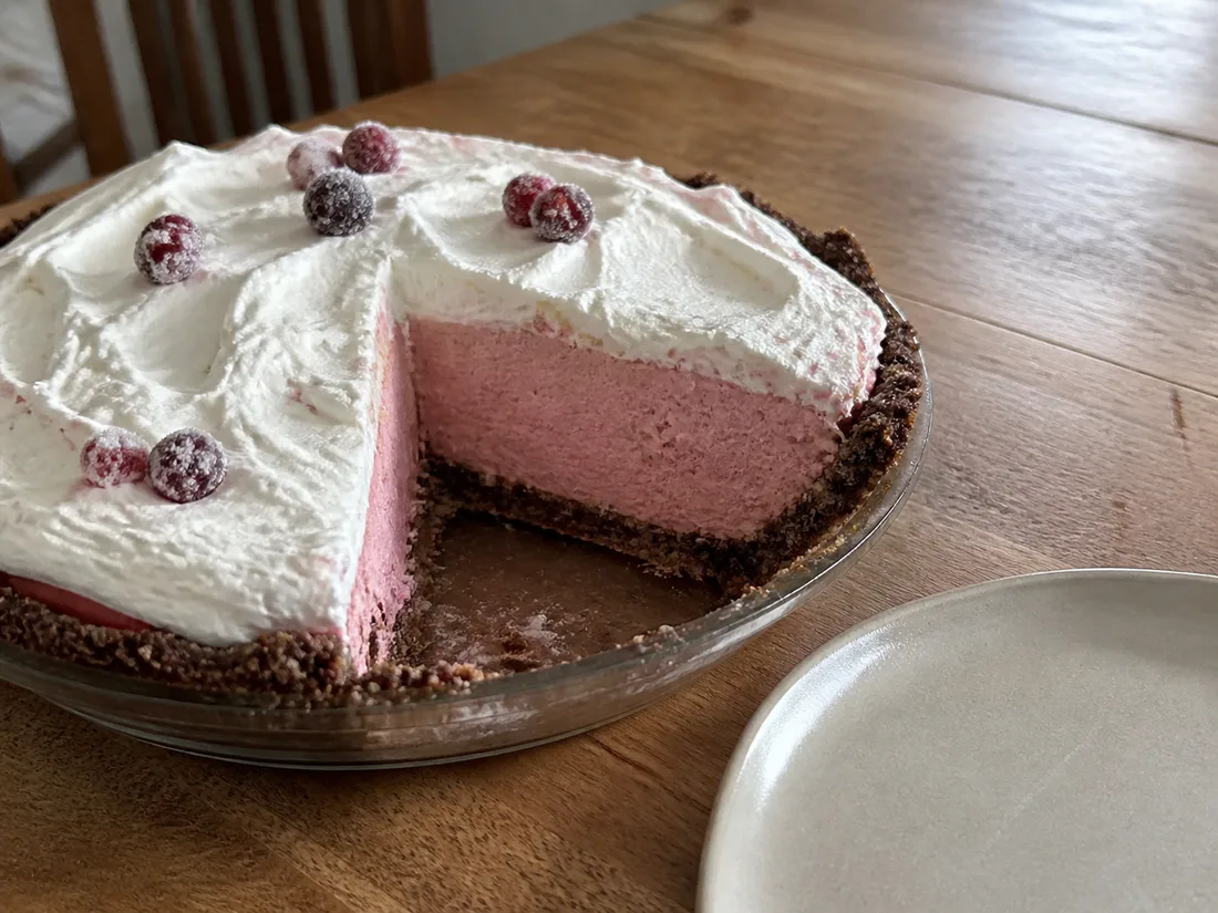 Pink cranberry chiffon pie in a dark rye crust with a soft cream topping.