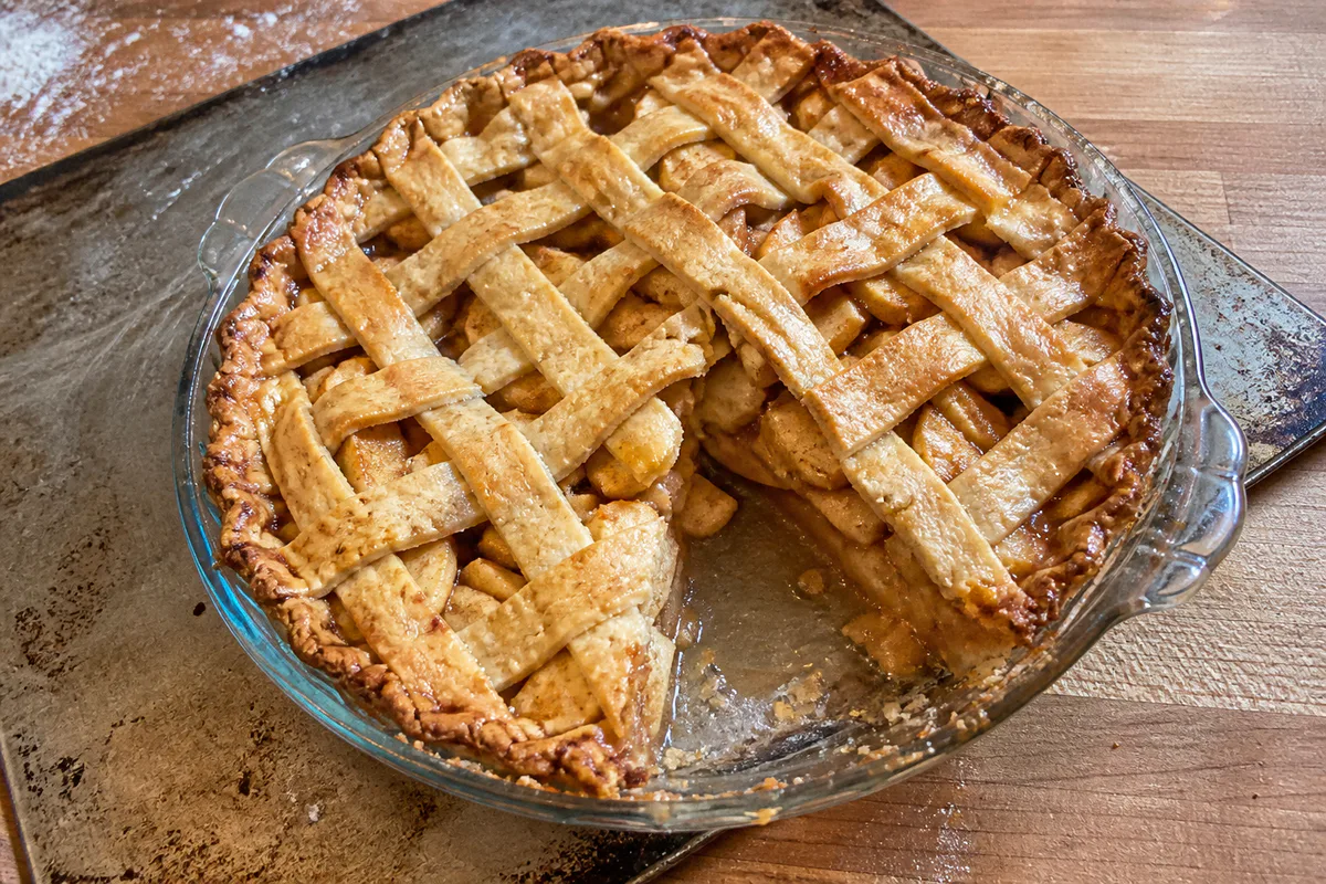Lattice-topped apple pie with visible cinnamon apples and an imperfect homemade crust.