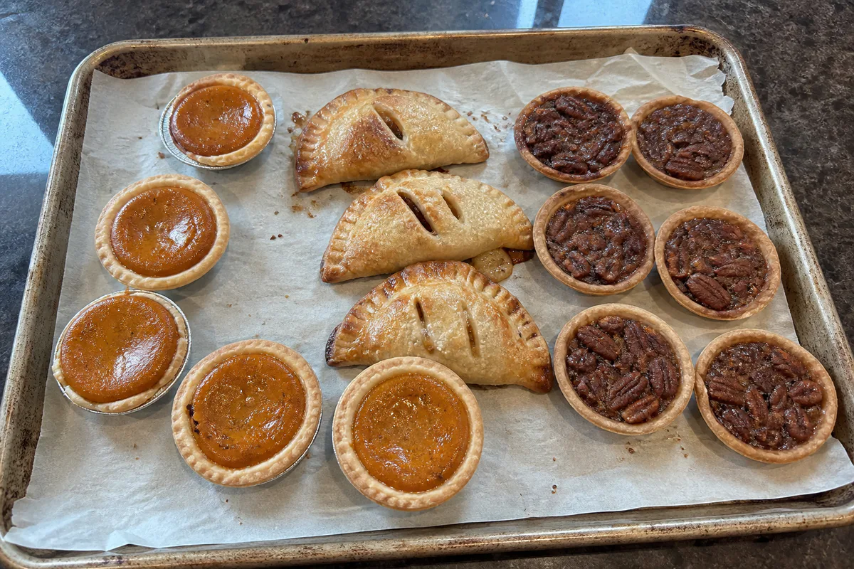 Tray of mini pumpkin pies, apple hand pies, and small pecan tarts for Thanksgiving.