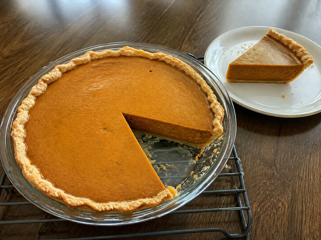 Classic pumpkin pie with a lightly cracked custard surface and a slice removed.