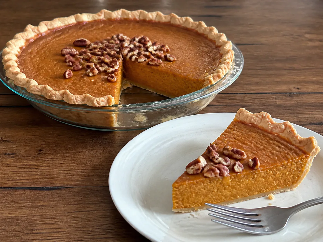 Sweet potato pie with a smooth orange filling, toasted pecans, and one slice removed.