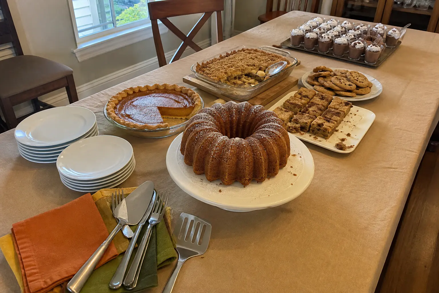 Thanksgiving dessert table arranged with a central Bundt cake, pies, bars, cookies, and serving tools.