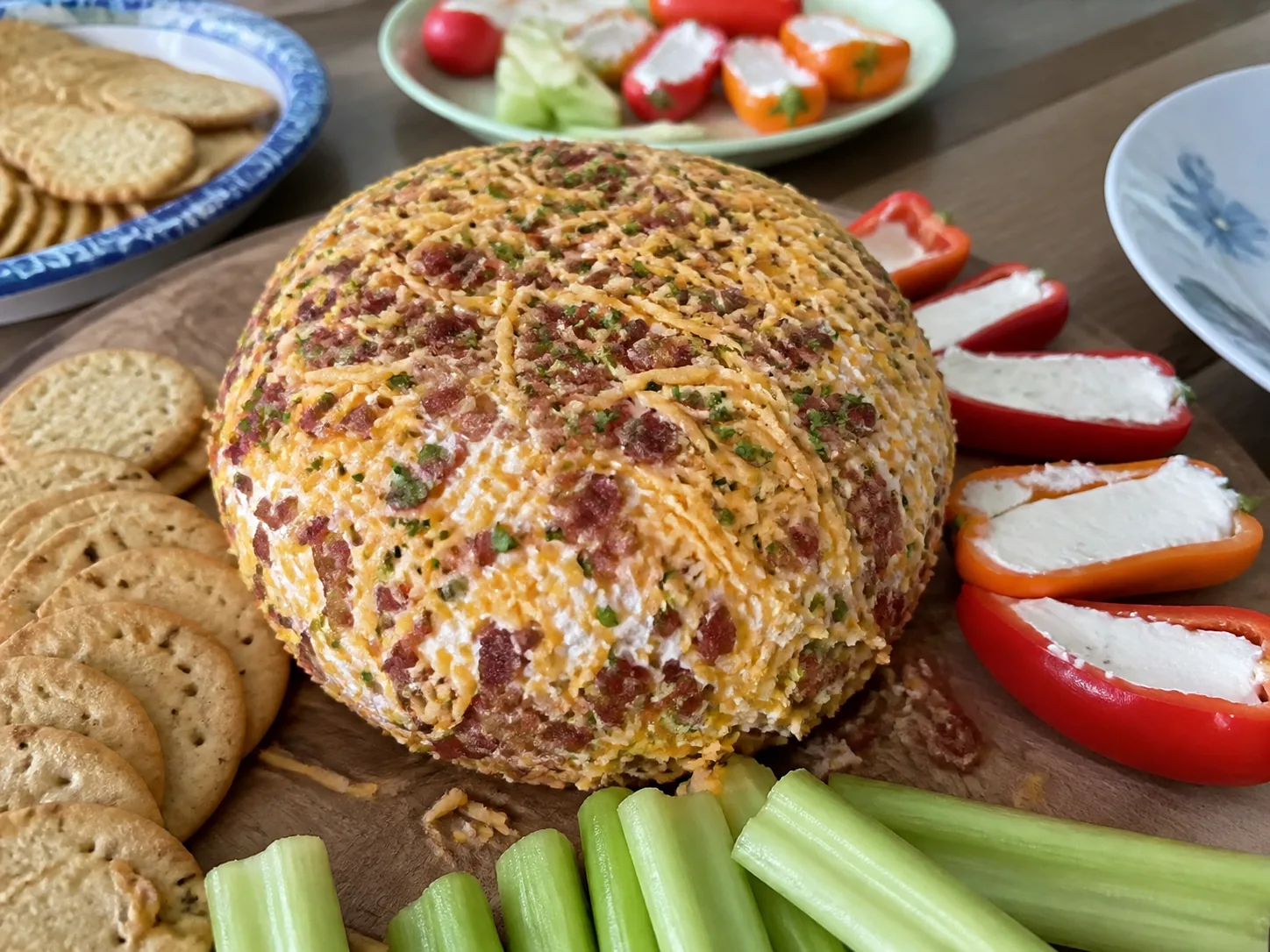 Homemade bacon cheddar cream cheese ball with crackers, stuffed mini peppers, and celery.