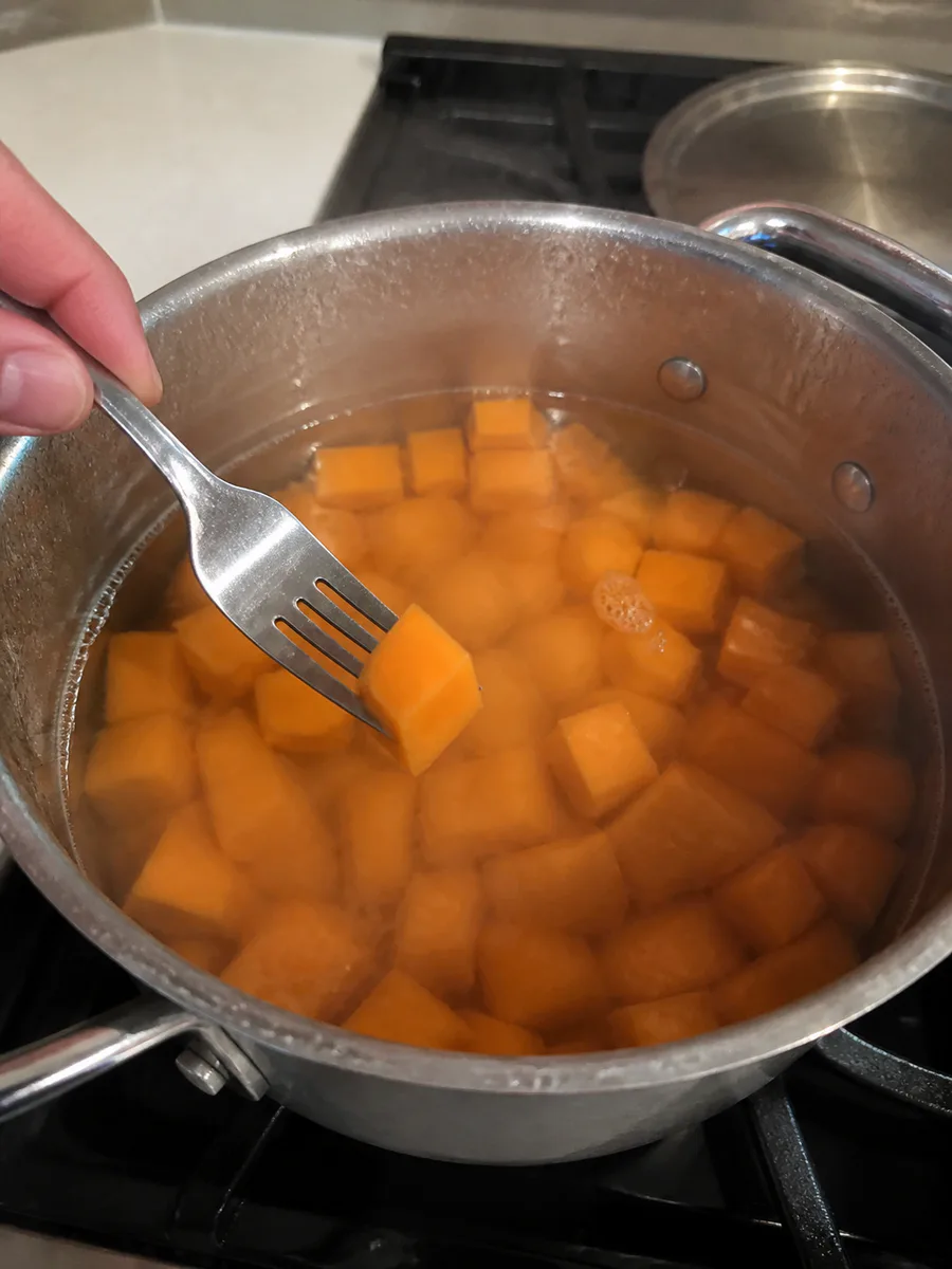 Cubed sweet potatoes simmering in a large pot while a fork checks for tenderness