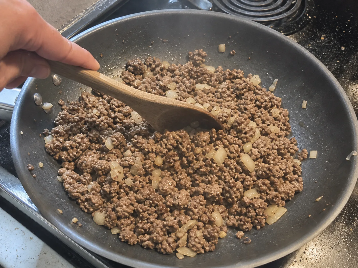 Ground beef and chopped onions browning in a skillet for cheeseburger casserole.