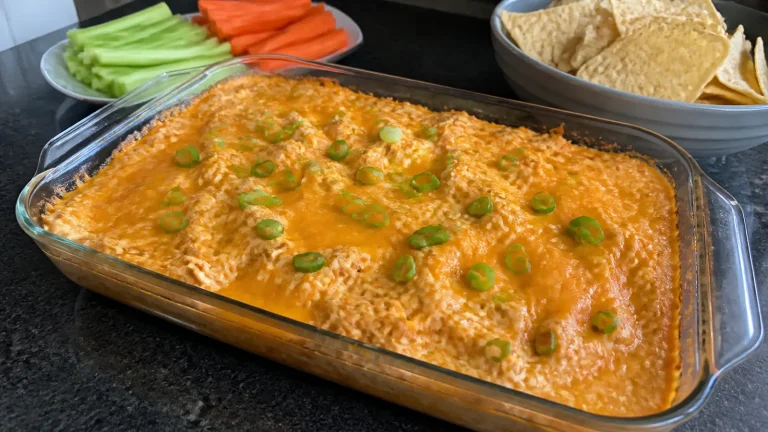 Baked buffalo chicken dip topped with melted cheddar and green onions beside celery, carrots, and tortilla chips