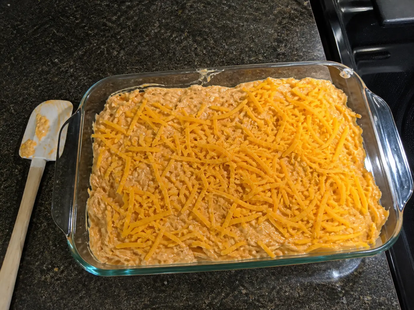Unbaked buffalo chicken dip spread in a glass baking dish and topped with cheddar