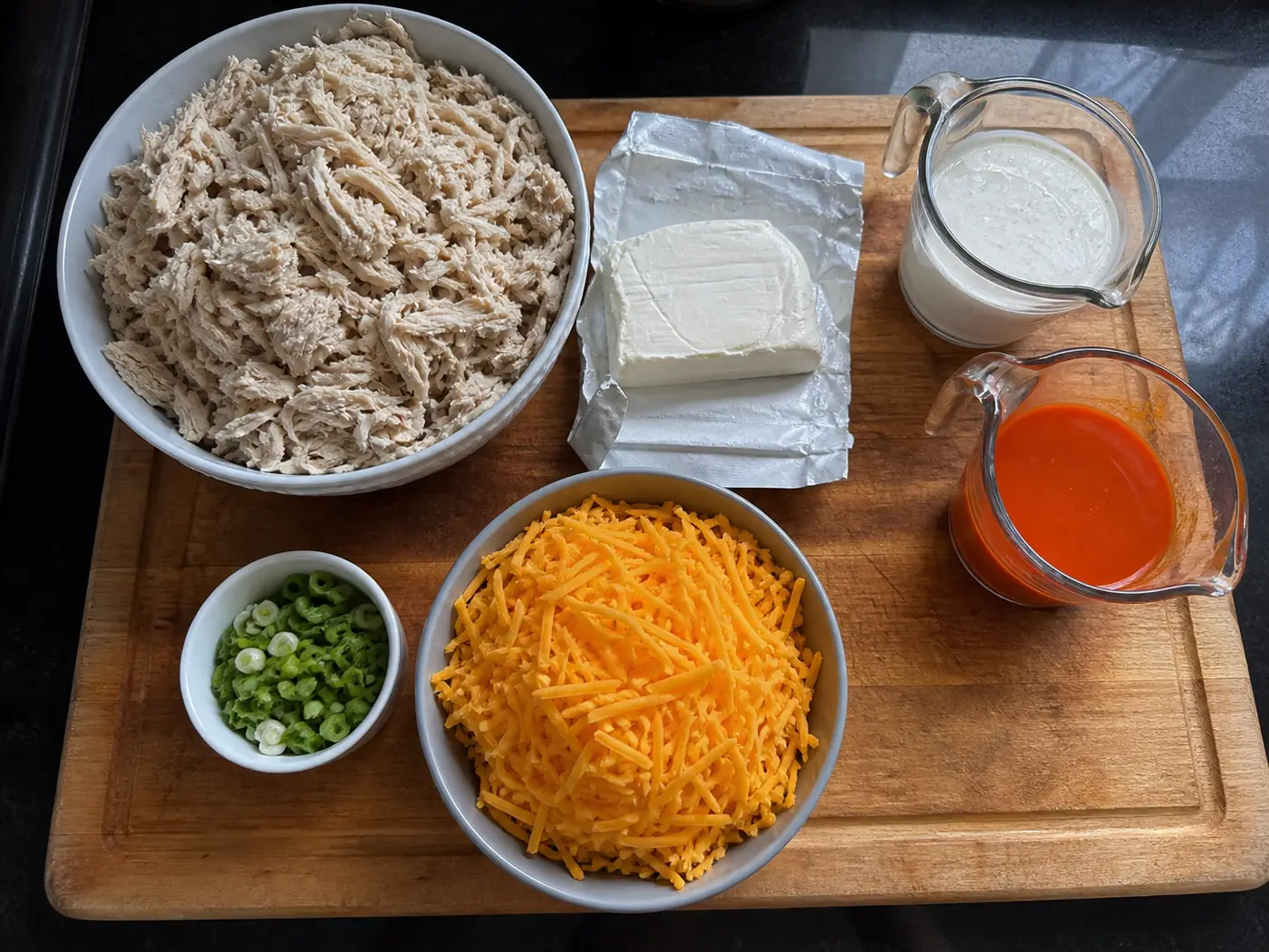 Buffalo chicken dip ingredients with shredded chicken, cream cheese, ranch, wing sauce, and grated cheddar