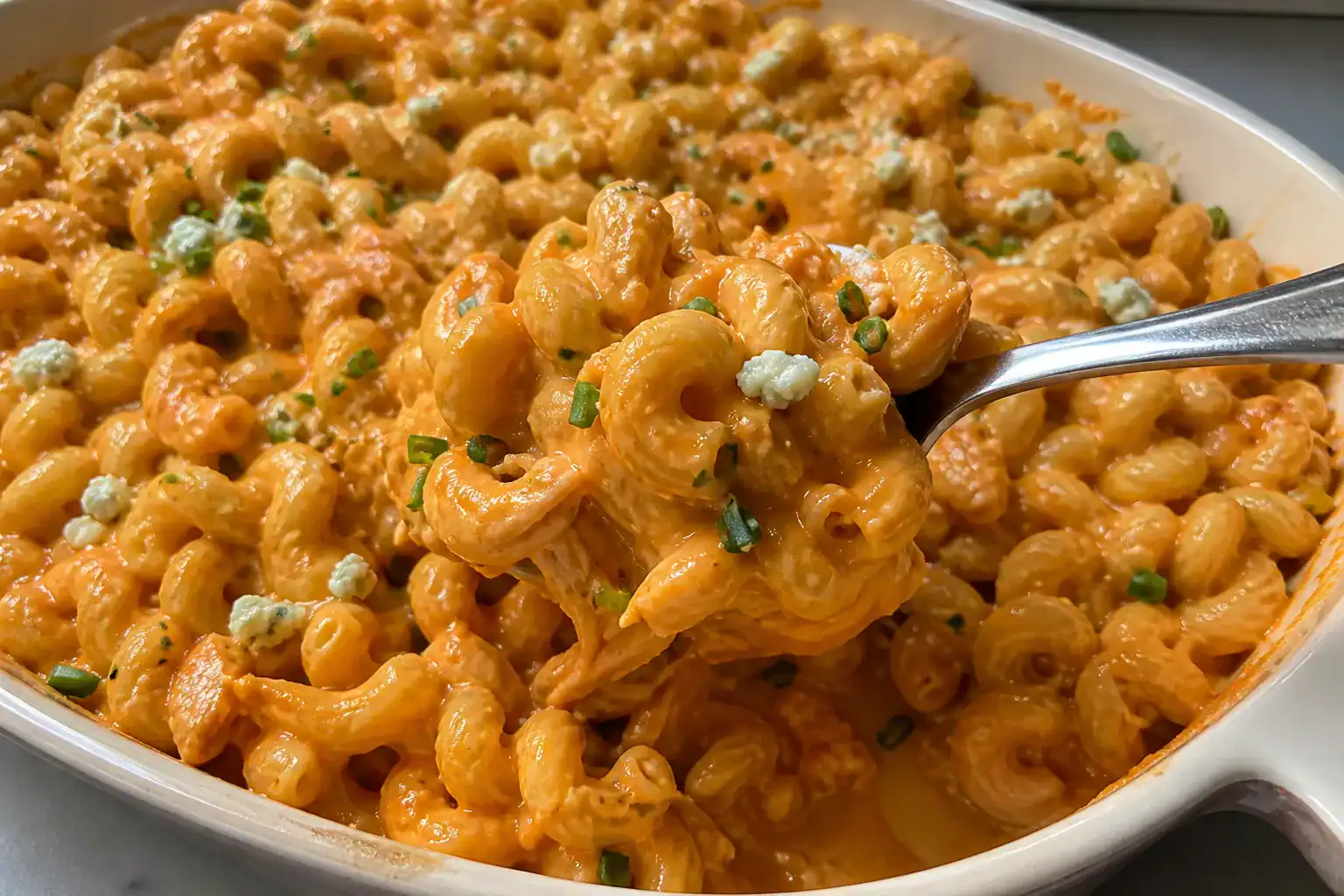 Spoonful of creamy buffalo chicken mac and cheese with cavatappi, shredded chicken, chives, and blue cheese.