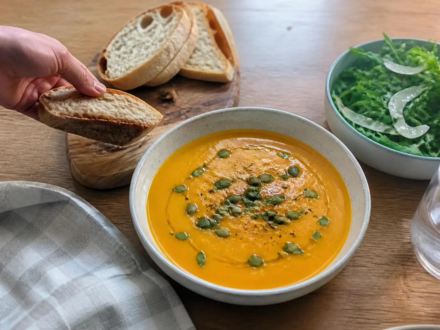 Butternut squash soup served with toasted pepitas, herbs, olive oil, salad, and crusty bread