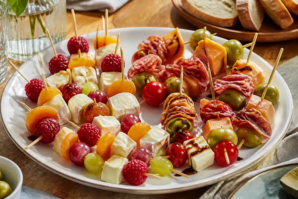 Mixed sweet and savory cheese skewers with fruit, olives, tomatoes, salami, and prosciutto on a party platter.