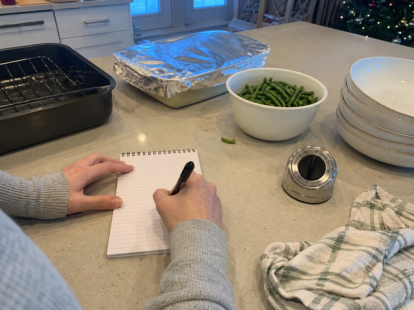 Home cook planning a Christmas dinner beside a roast, potato casserole, green beans, and serving dishes.