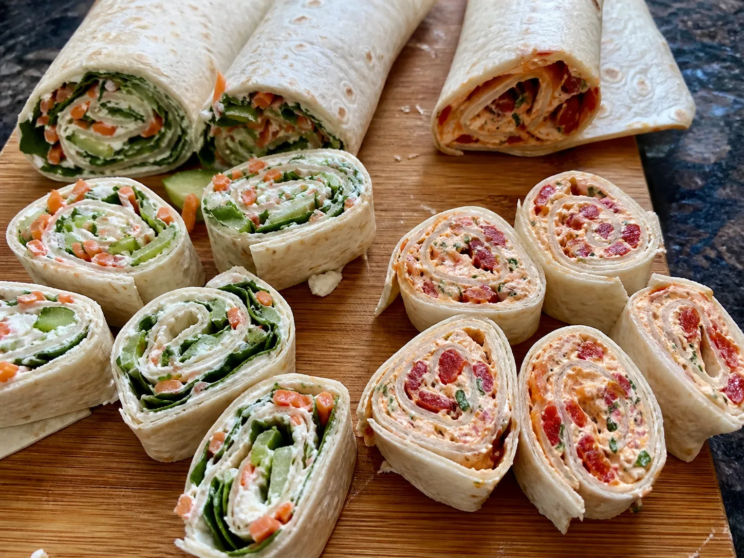 Ranch vegetable and roasted red pepper cream cheese tortilla pinwheels on a cutting board.