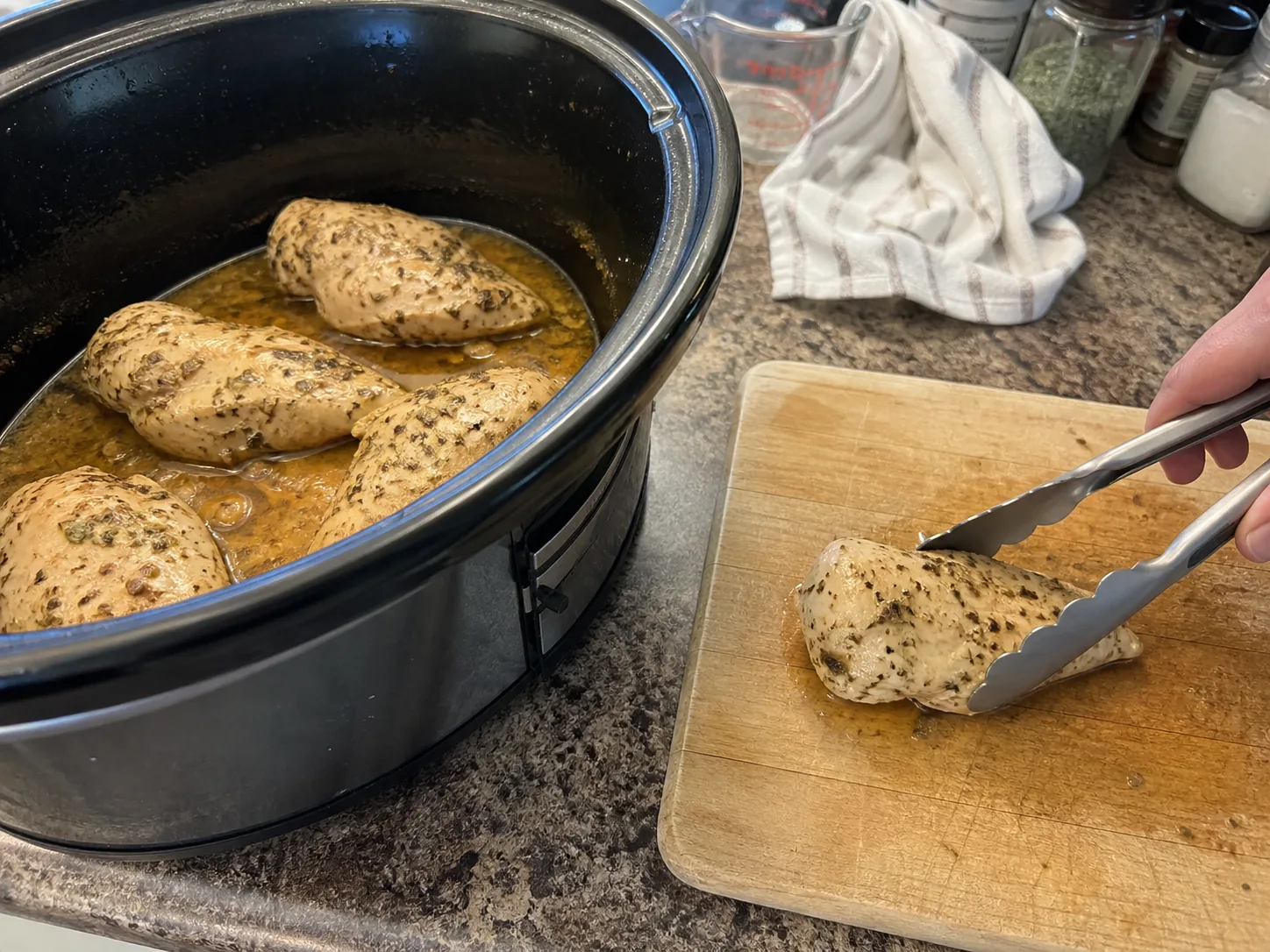 Removing cooked chicken breast from a slow cooker with tongs