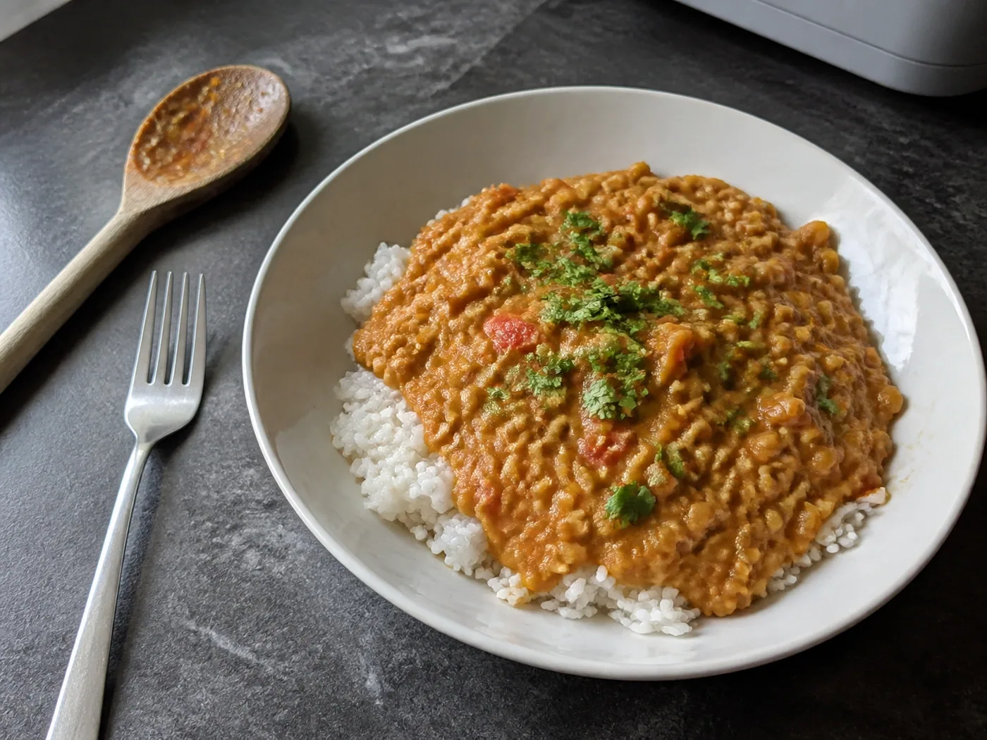 Red curry lentils with coconut milk served over white rice on a home kitchen table.