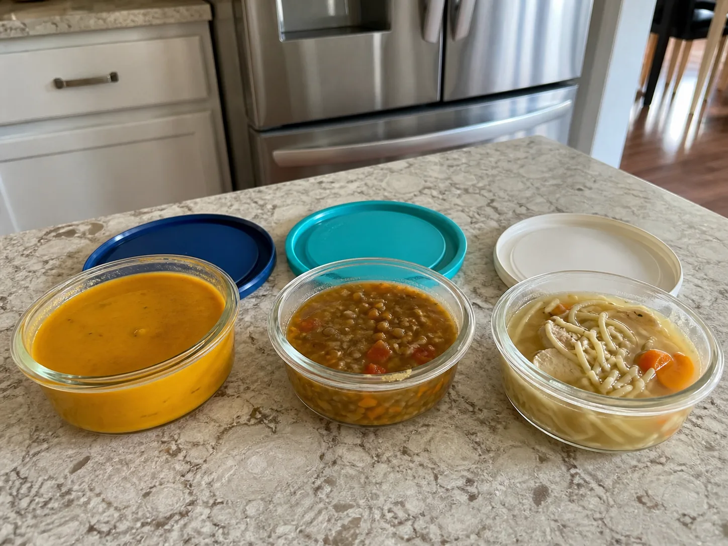 Squash, lentil, and chicken noodle soups portioned in shallow glass containers for refrigeration.