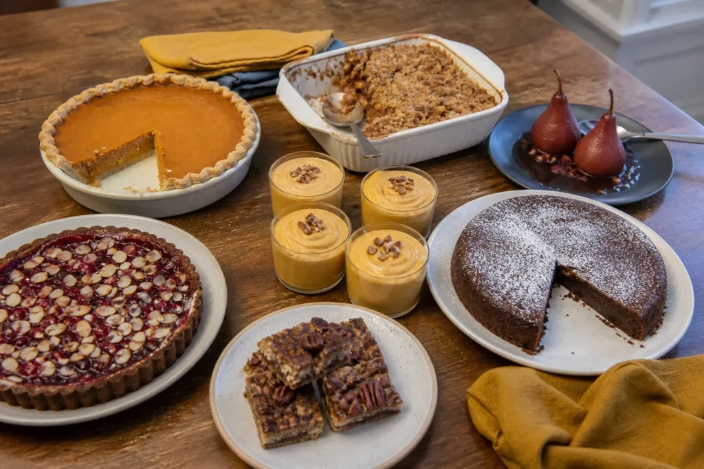 Gluten-free Thanksgiving dessert table with pumpkin pie, apple crisp, flourless chocolate cake, cranberry tart, mousse cups, pecan bars, and poached pears.