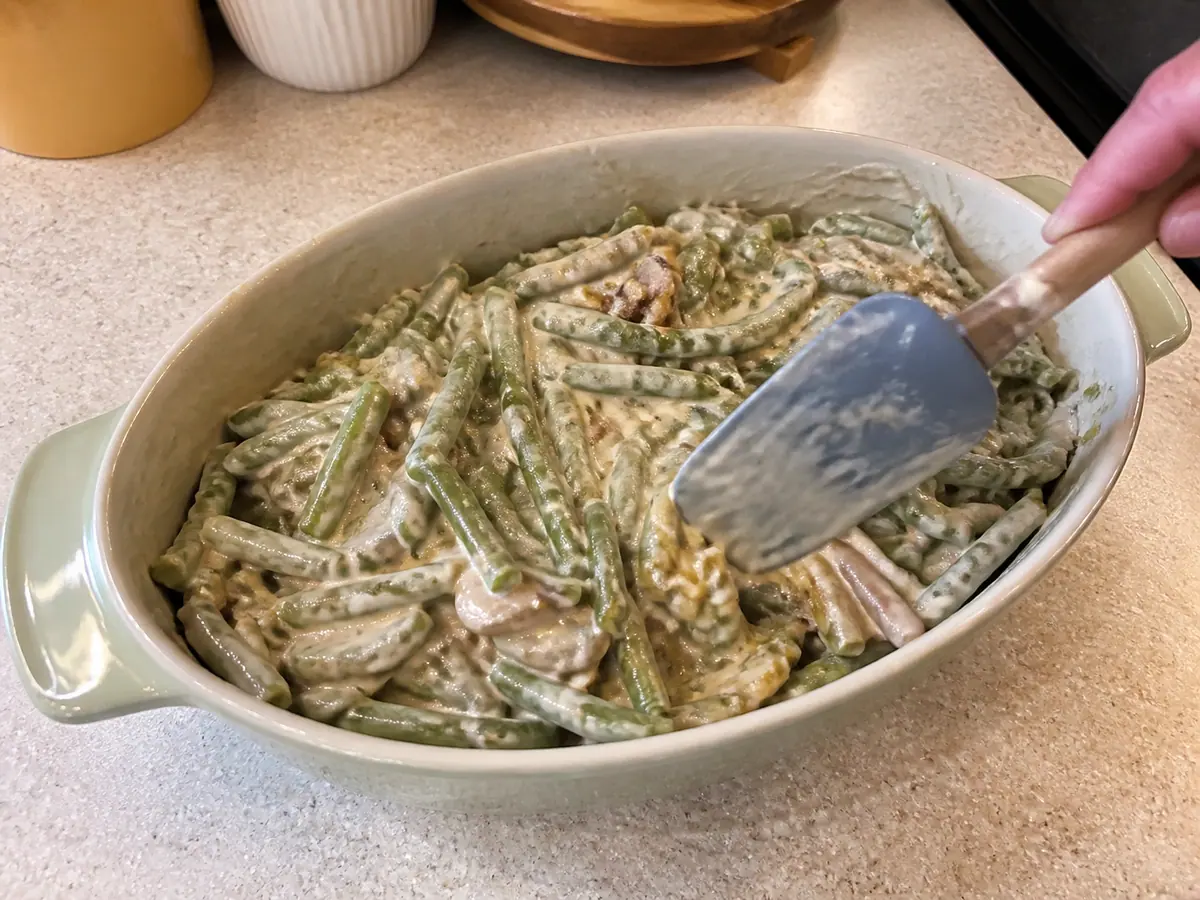 Green beans and fried onions folded into creamy mushroom sauce in a casserole dish before baking.