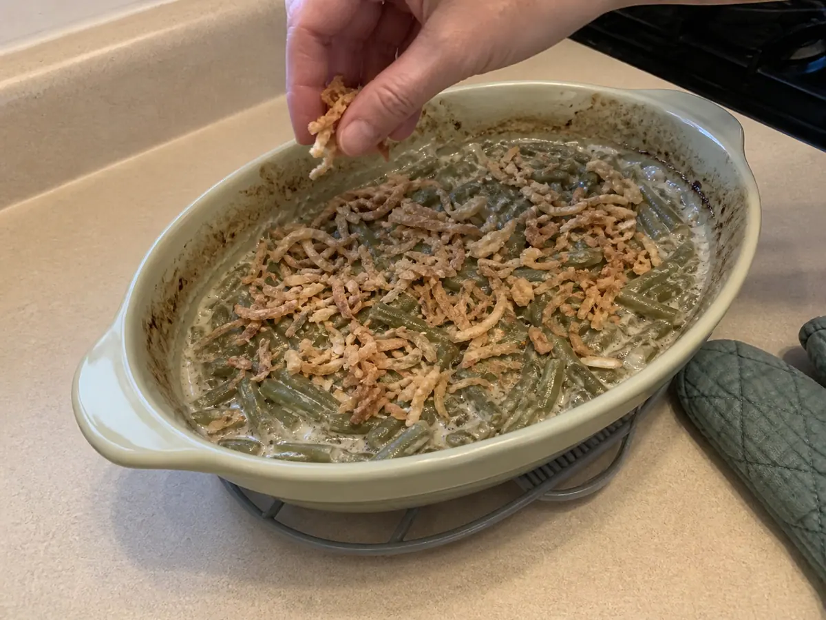 Golden crispy fried onions being added to green bean casserole for the final five minutes of baking.