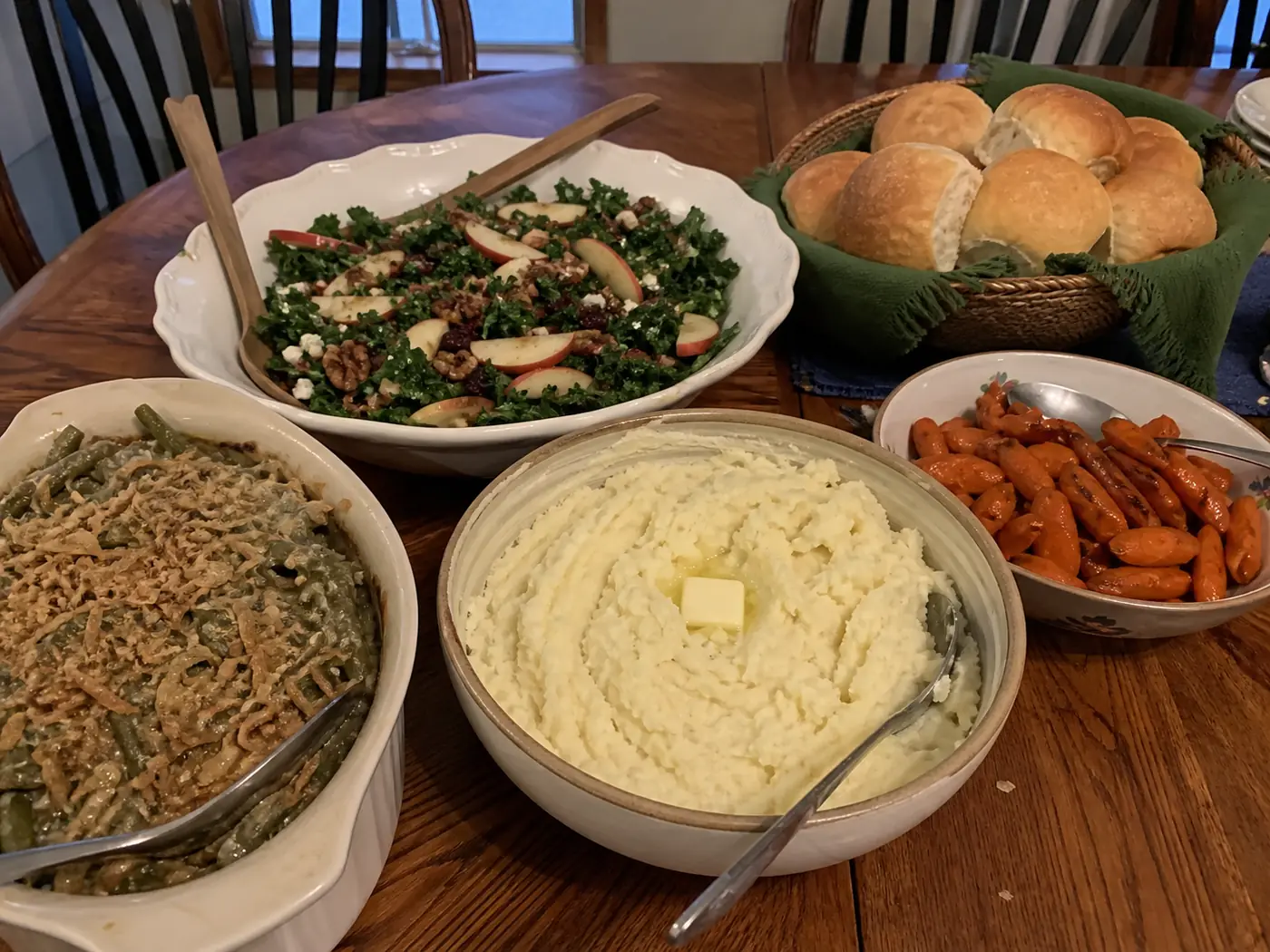 Mashed potatoes, green bean casserole, roasted carrots, winter salad, and dinner rolls on a holiday table