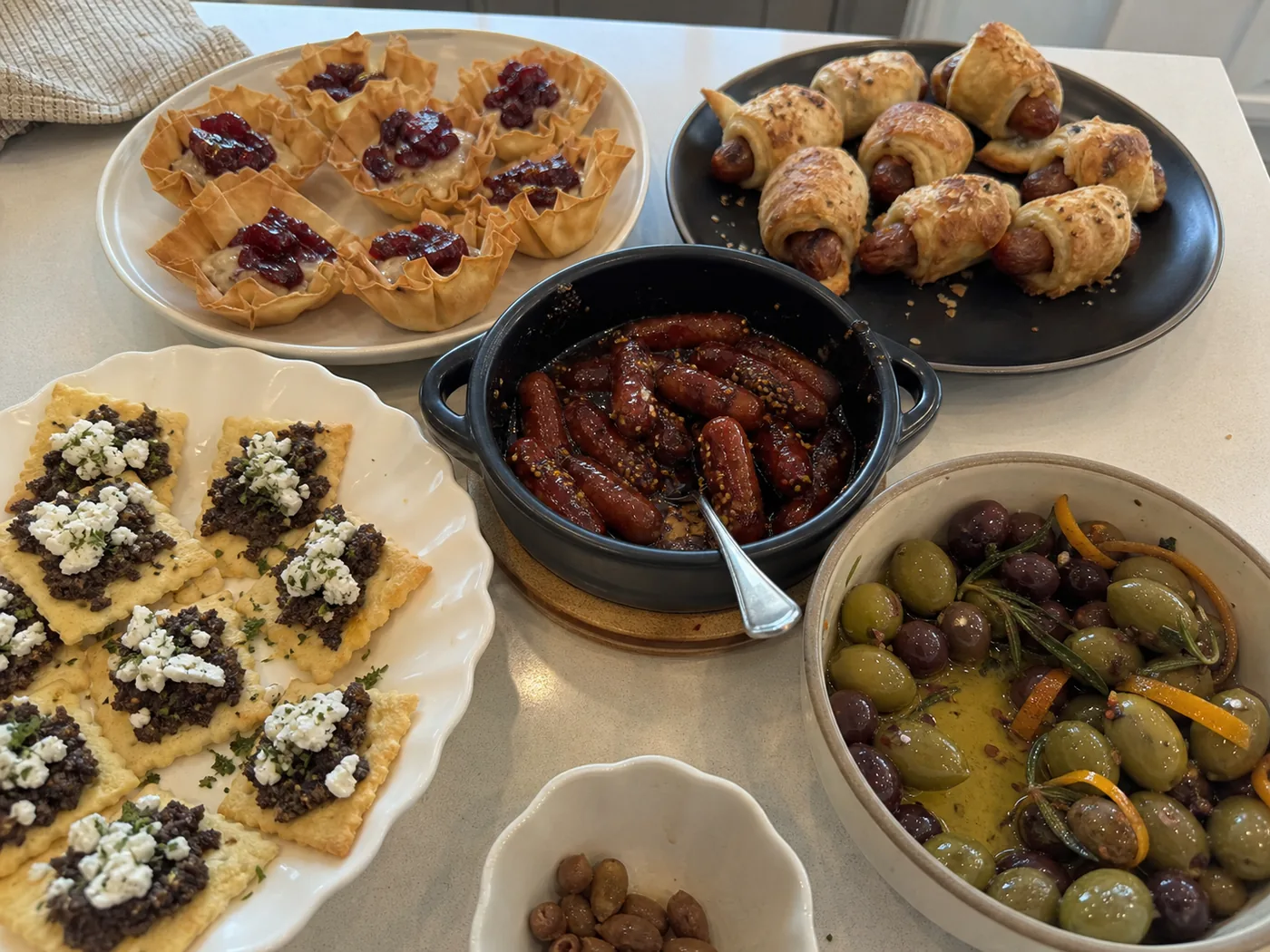 Brie cranberry phyllo cups, sausage crescent bites, tapenade crackers, cocktail sausages, and warm marinated olives