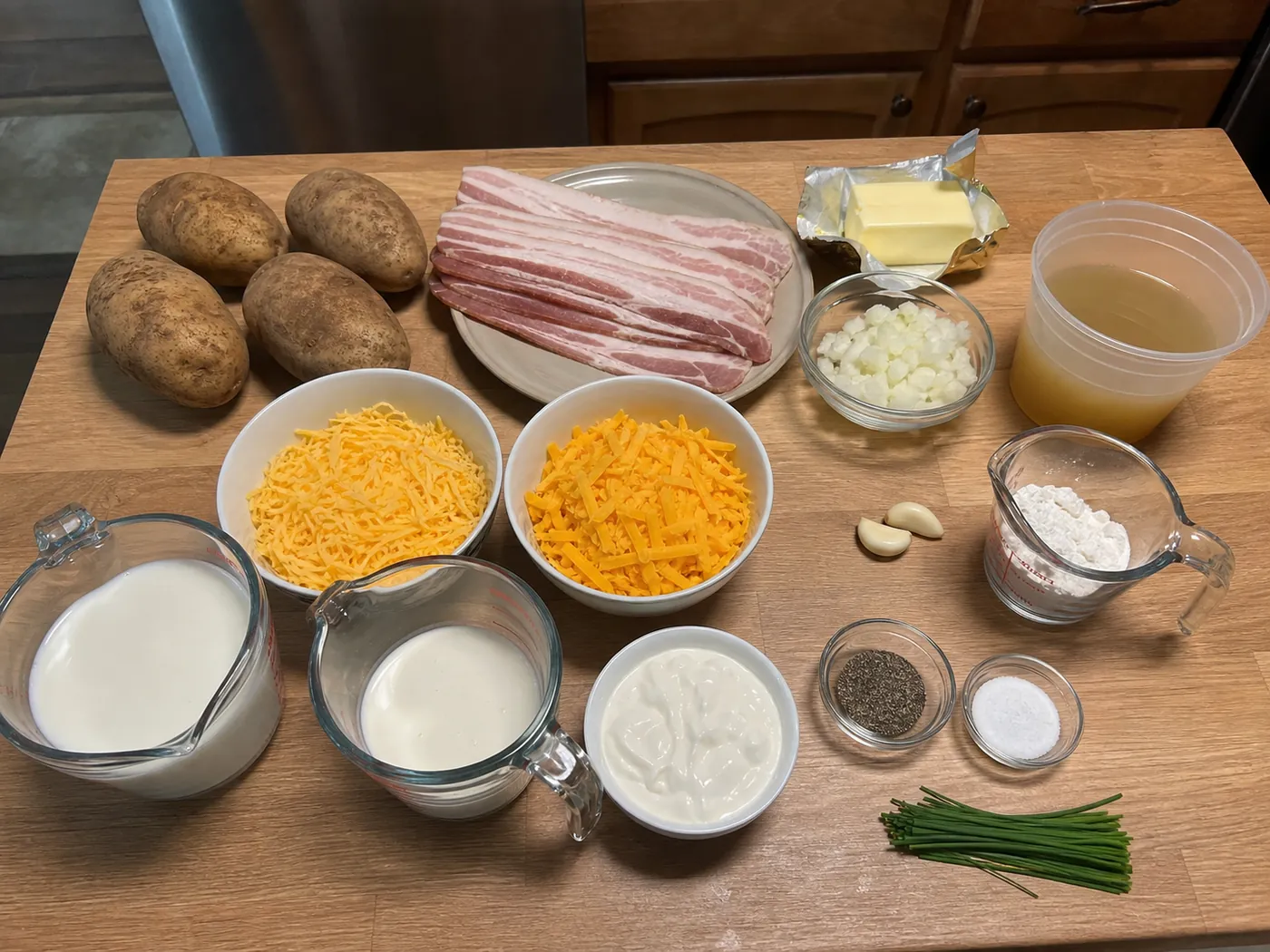 Loaded baked potato soup ingredients with potatoes, bacon, cheddar, sour cream, milk, stock, onion, and chives