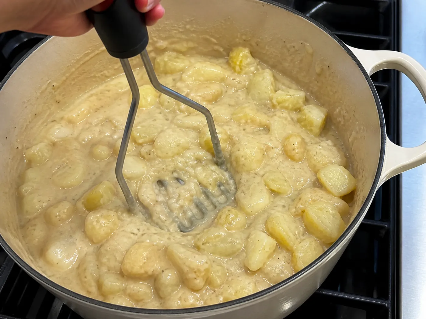 Potato pieces being partly mashed in creamy loaded baked potato soup