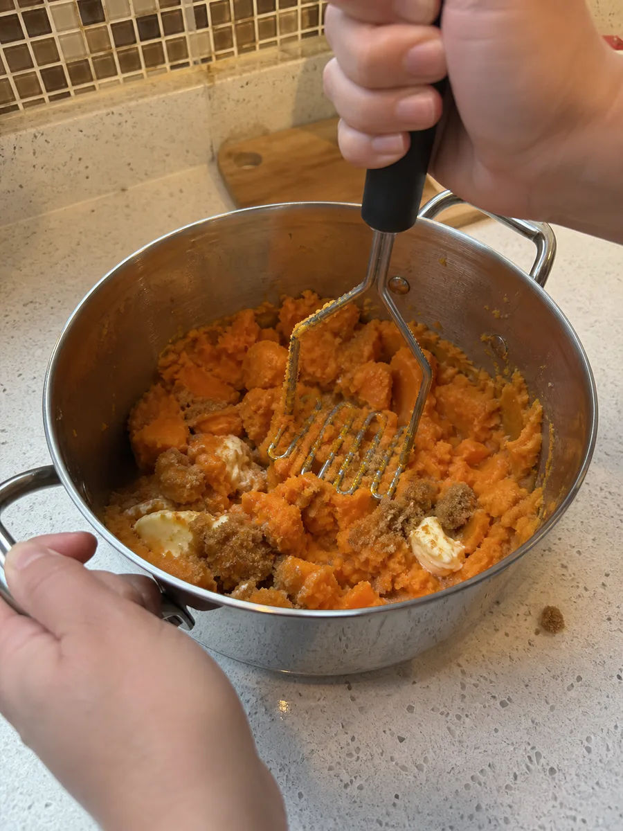 A home cook mashing warm sweet potatoes with butter, brown sugar, and cinnamon