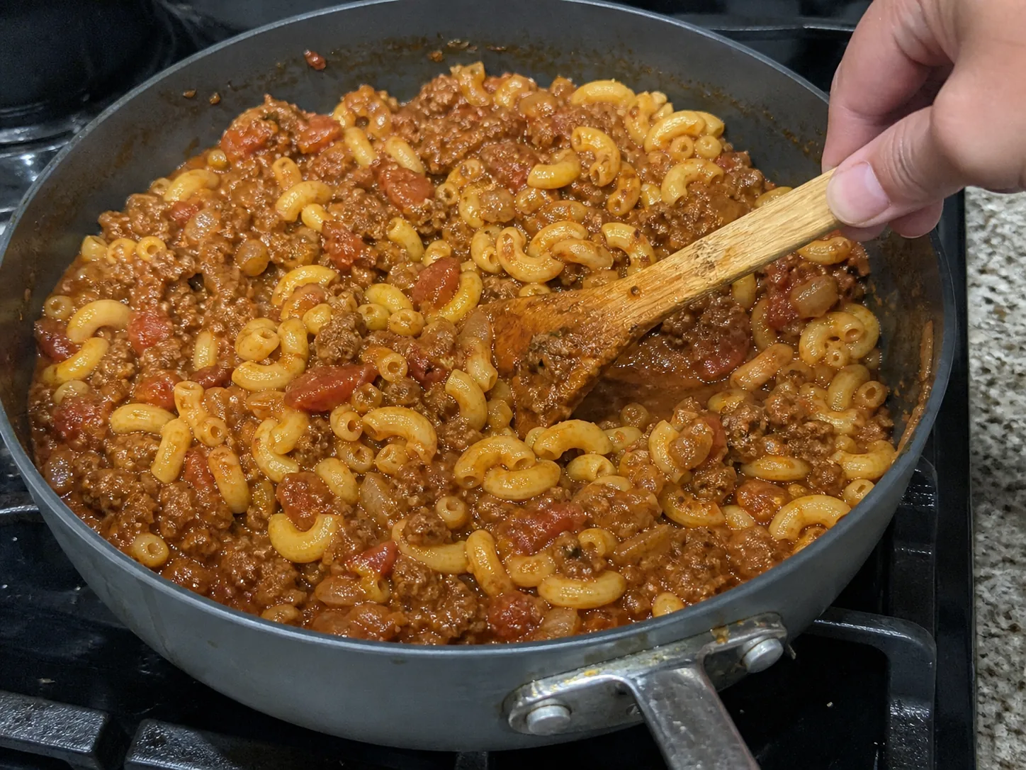 Cooked elbow macaroni folded into the ground beef and tomato sauce in a skillet.