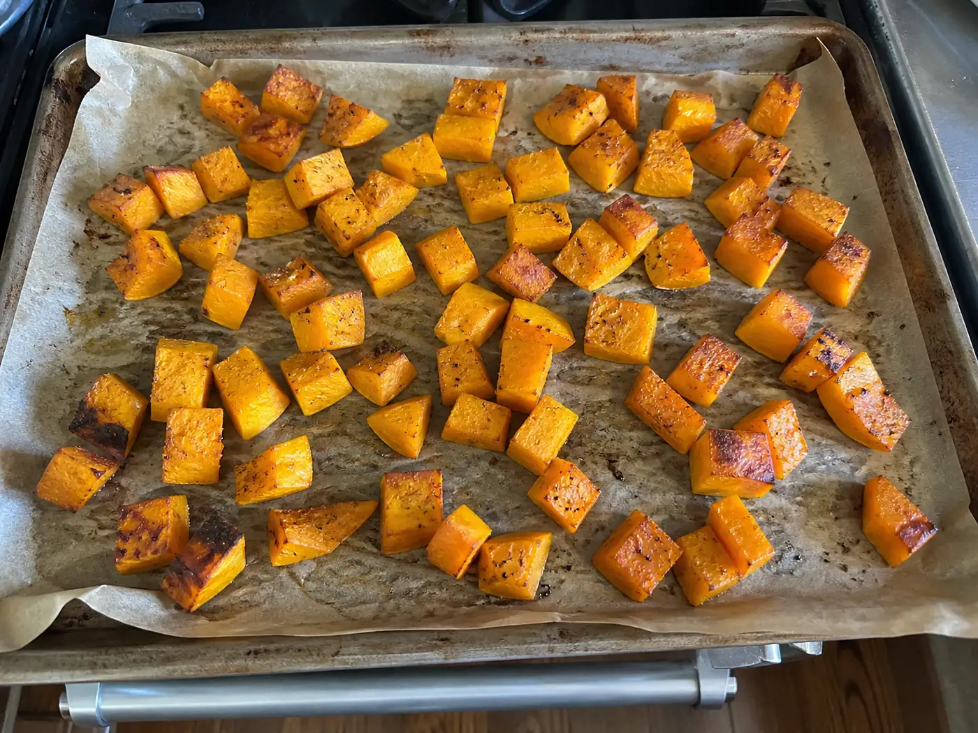 Roasted butternut squash cubes with caramelized edges on a parchment-lined sheet pan
