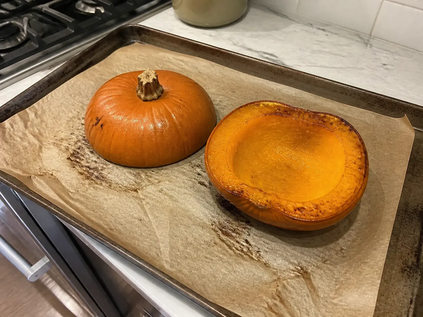 Roasted edible pumpkin halves on a parchment-lined sheet pan