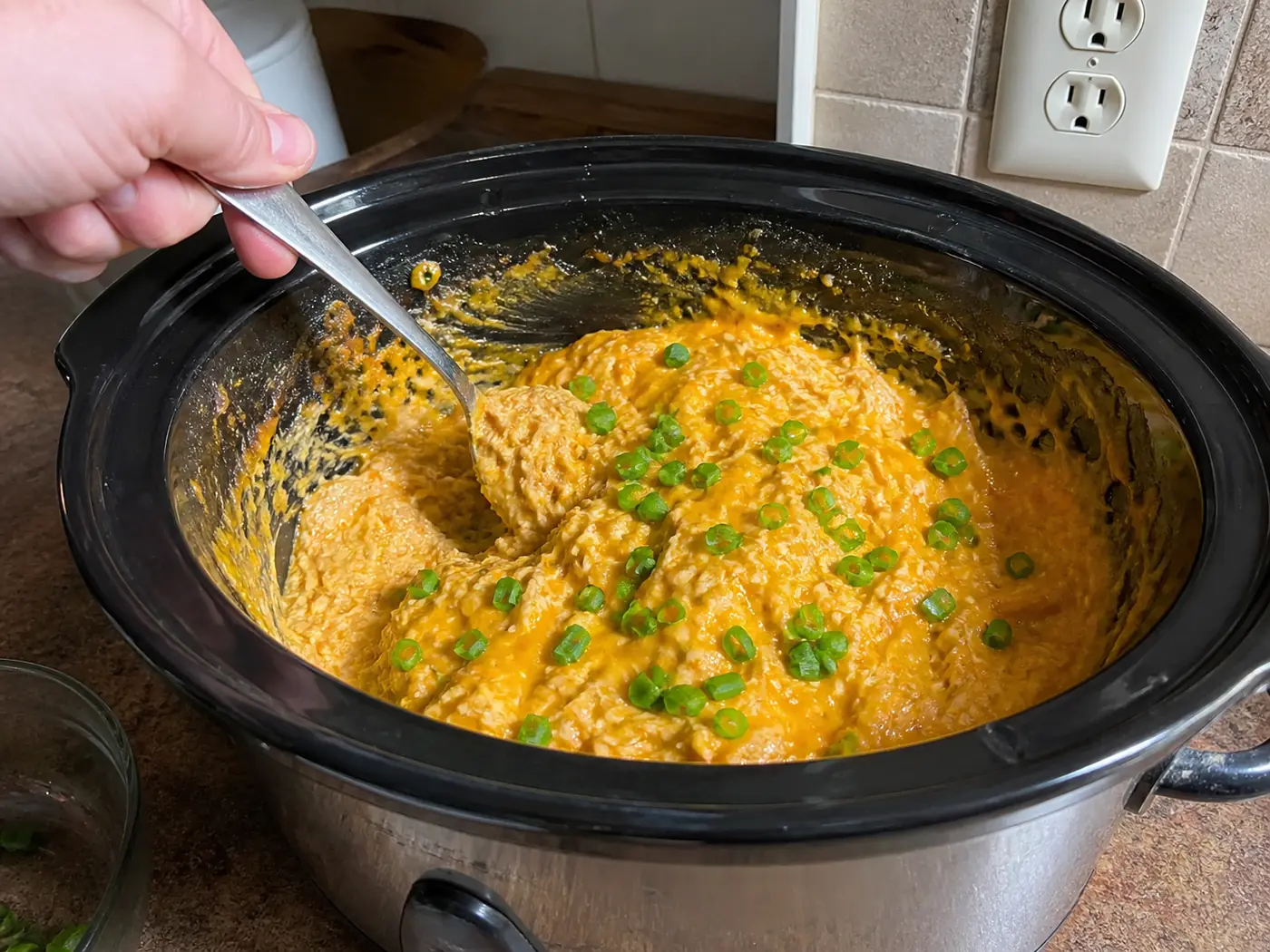 Buffalo chicken dip warming in a small slow cooker with a spoon beside it