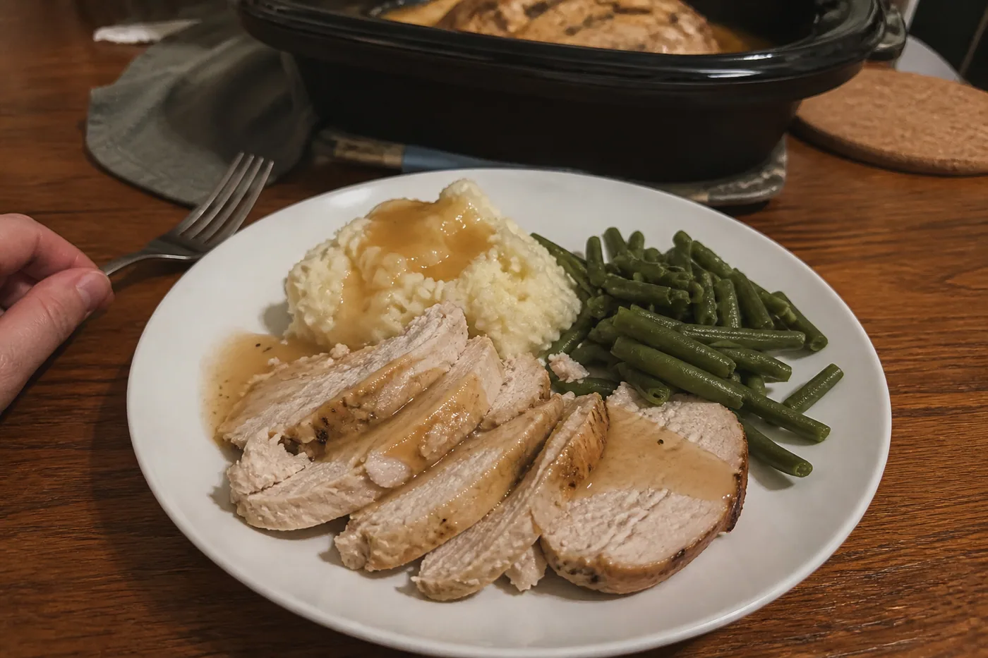 Sliced slow cooker turkey breast with gravy, mashed potatoes, and green beans.