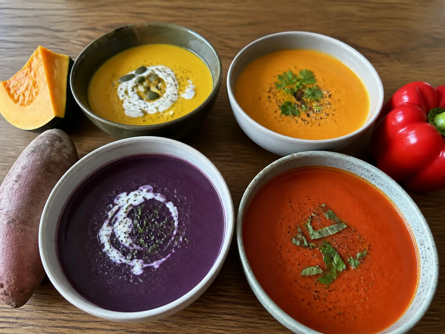 Butternut squash, pumpkin, sweet potato, and roasted red pepper soups in four bowls.