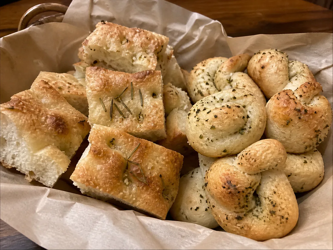 Basket of rosemary focaccia squares and herb garlic knots on a Thanksgiving table.