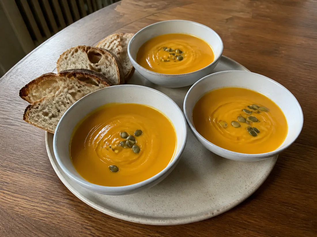 Small bowls of creamy butternut squash soup served with pepitas and slices of bread.