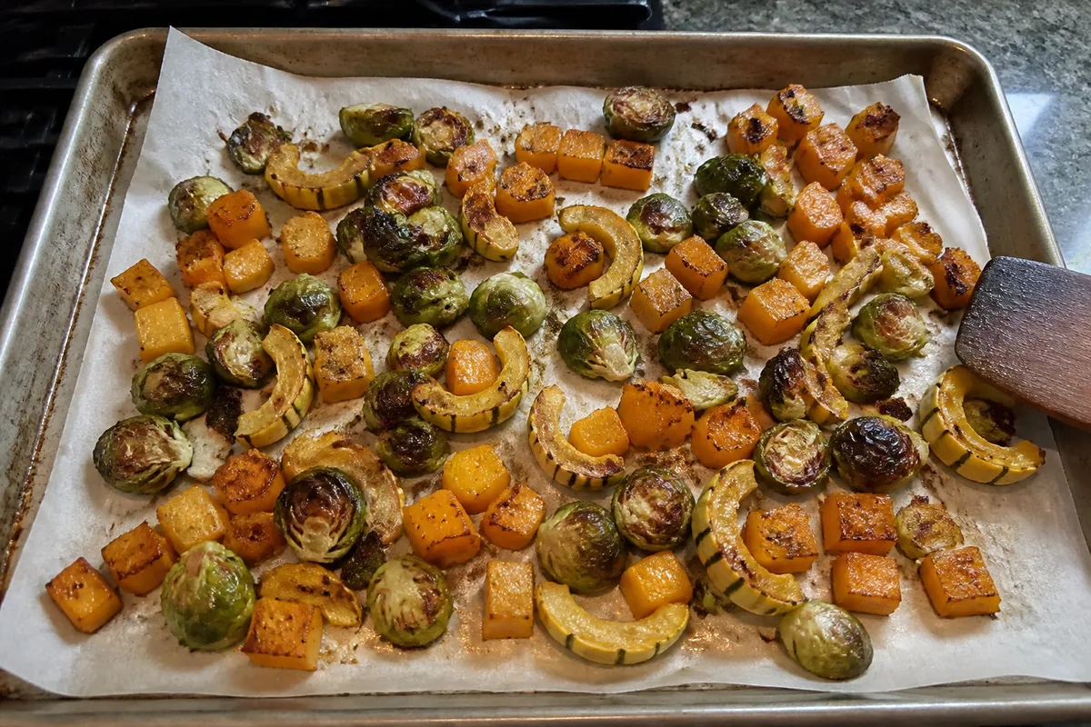 Sheet pan of maple-balsamic Brussels sprouts and roasted fall squash with browned edges.