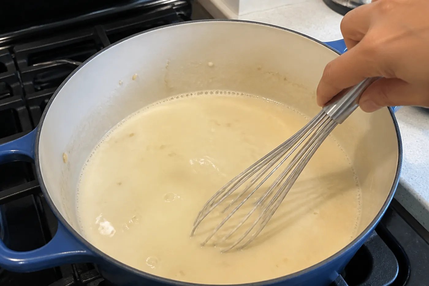 Creamy potato soup base being whisked at a gentle simmer in a Dutch oven
