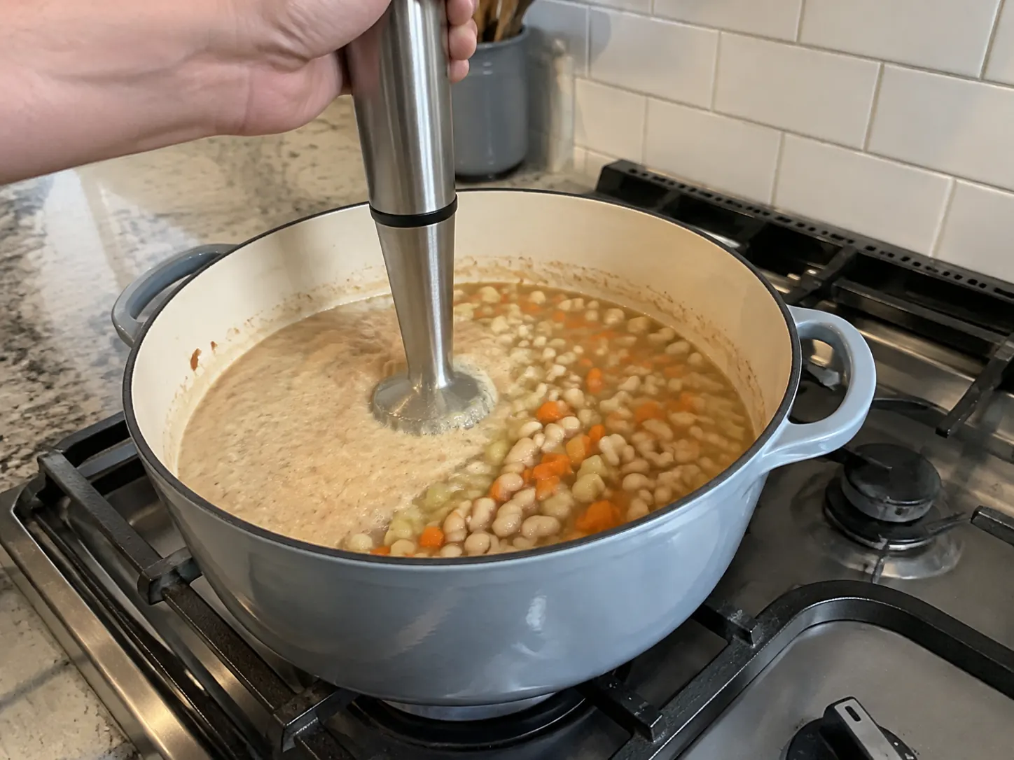 Immersion blender partially blending white beans and vegetables to thicken the soup naturally.