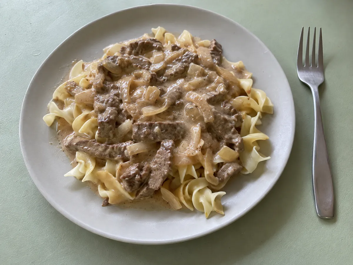 Beef strips in creamy sauce served over egg noodles on a gray plate.
