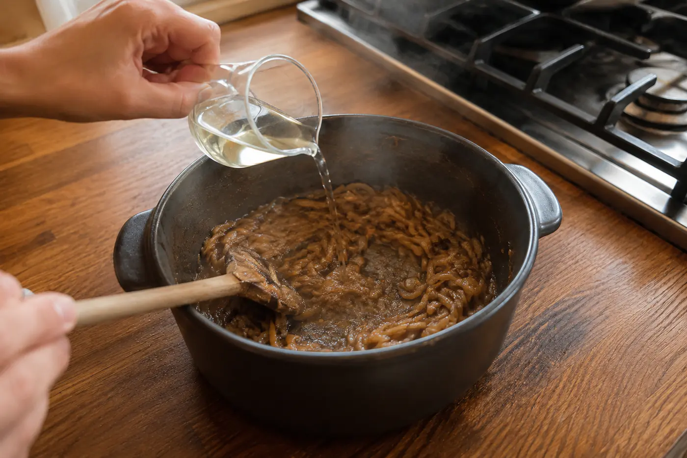 Dry white wine being poured into caramelized onions to deglaze the Dutch oven
