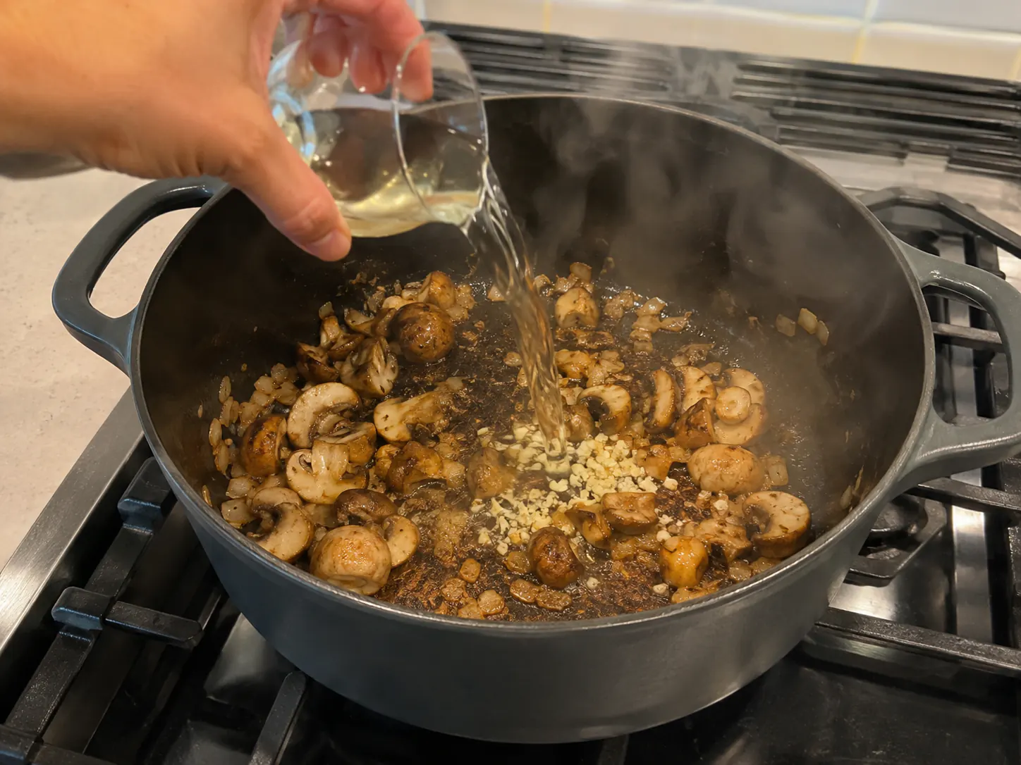 Dry white wine being poured over browned mushrooms and garlic to deglaze the soup pot.