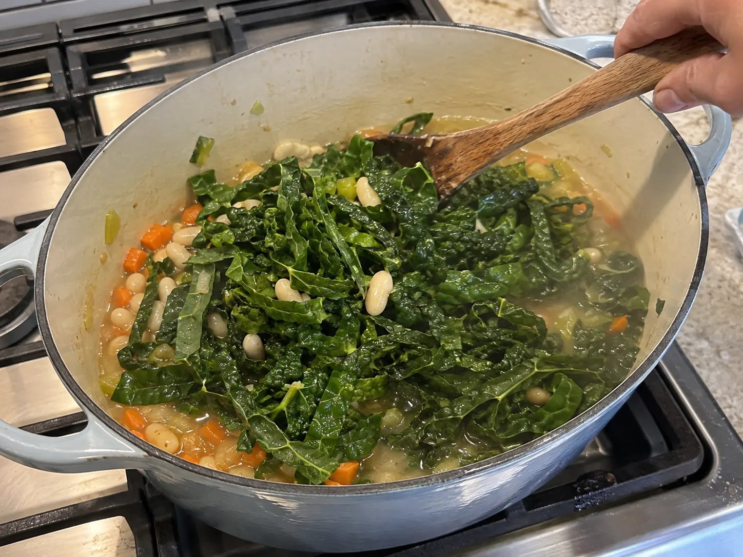 Chopped kale being folded into creamy white bean soup with a wooden spoon.