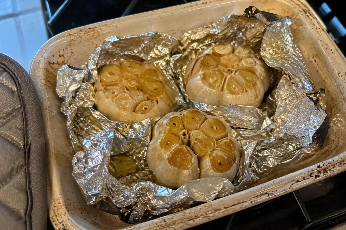 Golden roasted garlic heads opened in foil after baking until soft and caramelized.
