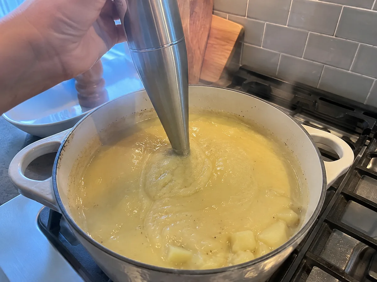 Immersion blender puréeing roasted garlic and potato soup directly in the pot.