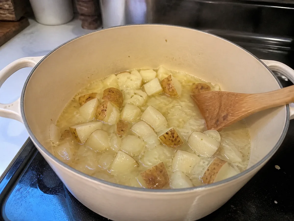 Chopped onion and potatoes simmering in broth in a home kitchen pot.