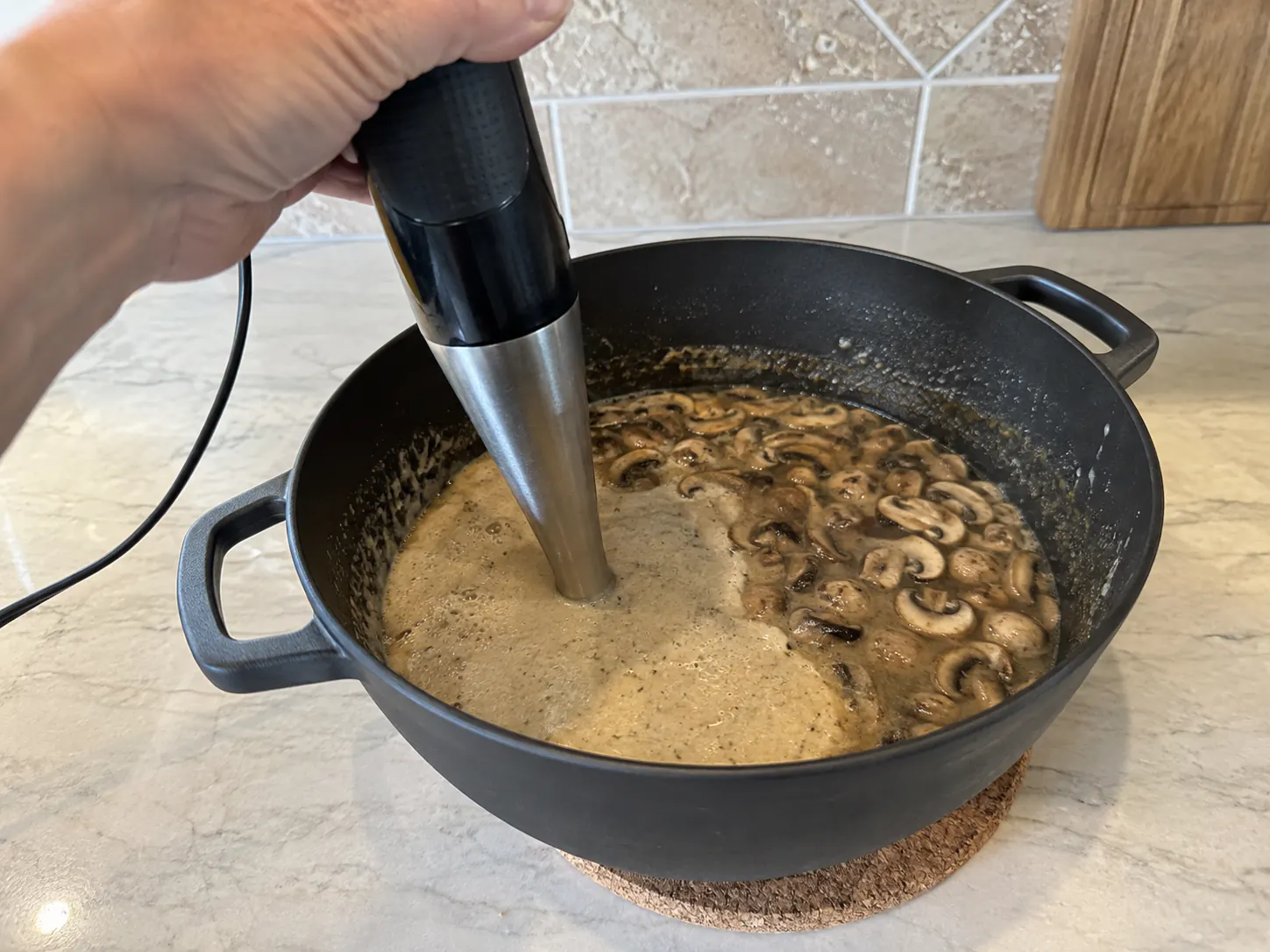 An immersion blender partially blending mushroom soup while some sliced mushrooms remain whole.