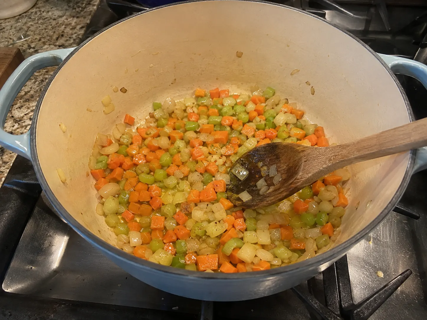Onion, carrots, and celery softening in olive oil in a pale blue-gray Dutch oven.